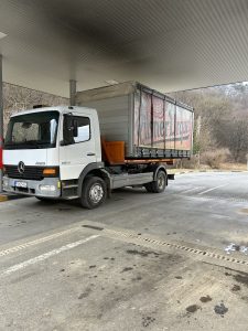 Nákladné vozidlo Mercedes Atego s kontajnerom pre prepravu ťažkých nákladov na čerpacej stanici. Vozidlo využívané spoločnosťou po-bagrujem.sk na prepravu zariadení a materiálov potrebných pre zemné práce, výkopové práce a úpravy terénu na rôznych stavbách a projektoch.