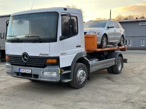 Nákladné vozidlo Mercedes Atego prepravujúce osobné auto na odťahovej plošine. Ideálne pre odvoz vozidiel a podporu zemných a výkopových prác v oblasti stavebníctva. Preprava strojov a zariadení je súčasťou služieb spoločnosti po-bagrujem.sk, ktorá sa špecializuje na zemné práce, výkopové práce a úpravy terénu.